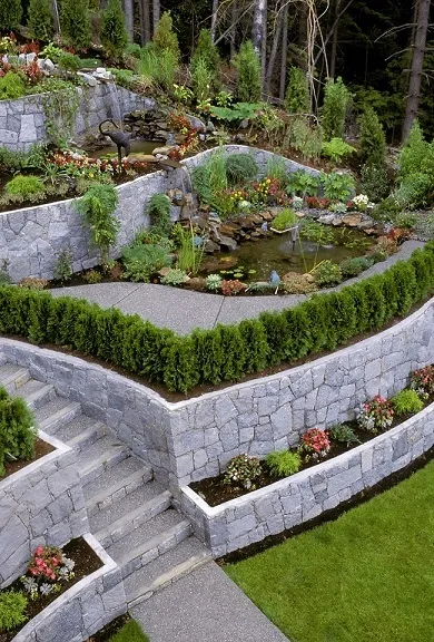 Tiered natural stone retaining walls with garden beds, a pond and stone steps on a terraced slope