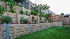 Tiered concrete sleeper retaining wall with garden planting along a backyard fence line