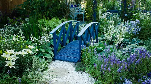 Ornamental garden bridge over a gravel path surrounded by flowering plants